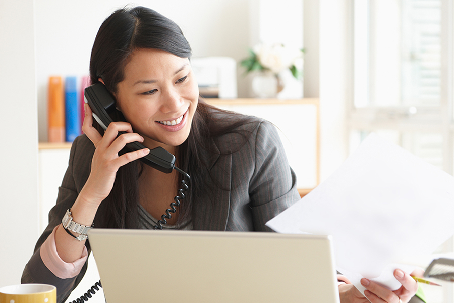 woman on the phone in front of her computer smiling a reviewing documents