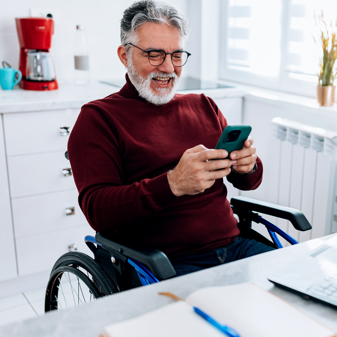 a smiling man in a wheelchair infront of his computer reading his text messages