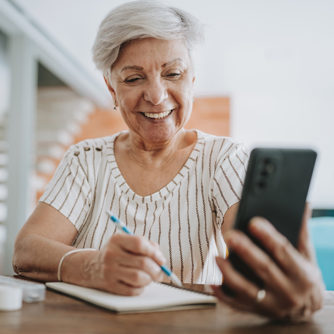 Elderly woman looking at resources on her phone and taking notes in notebook