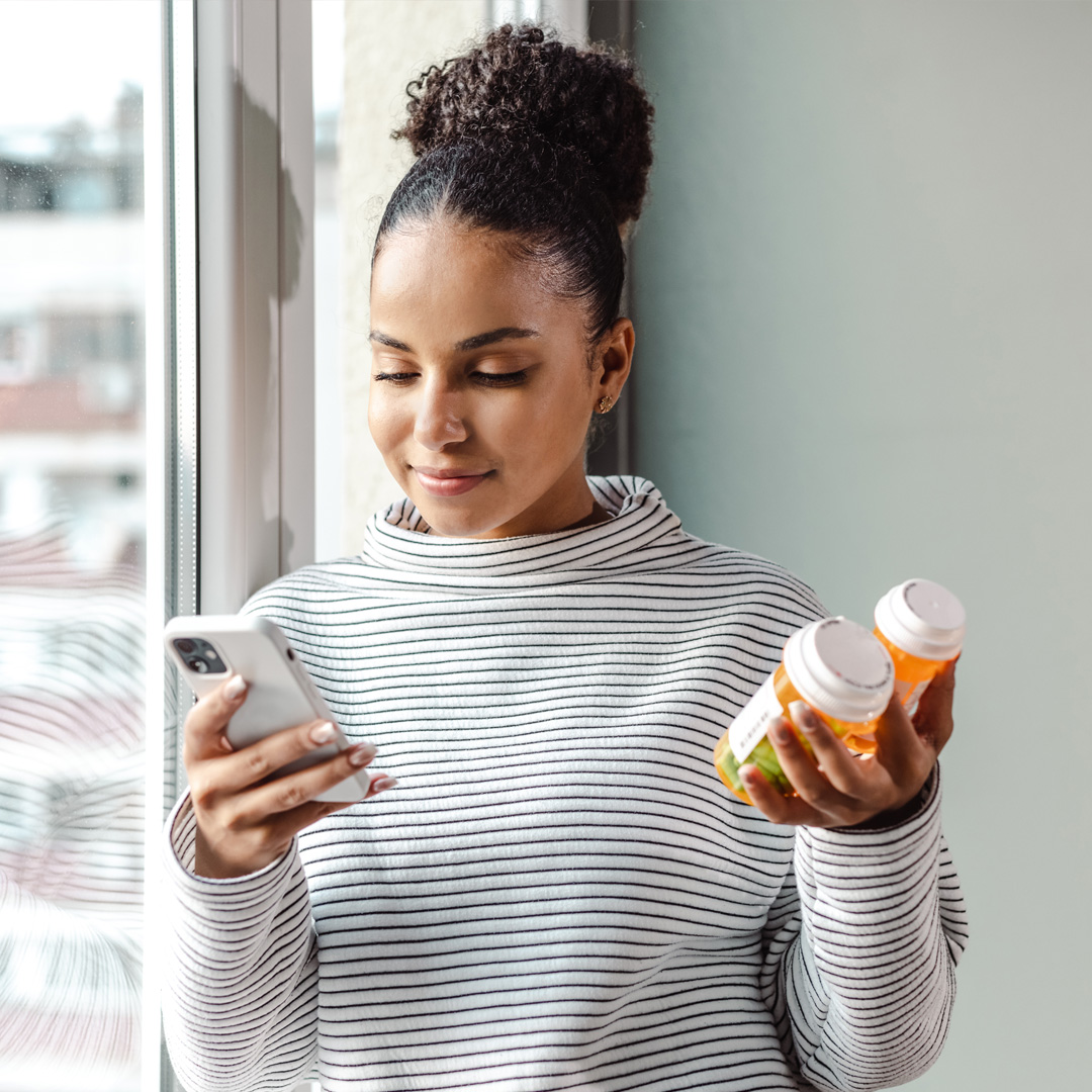 Young woman reading text messages and holding her prescriptions